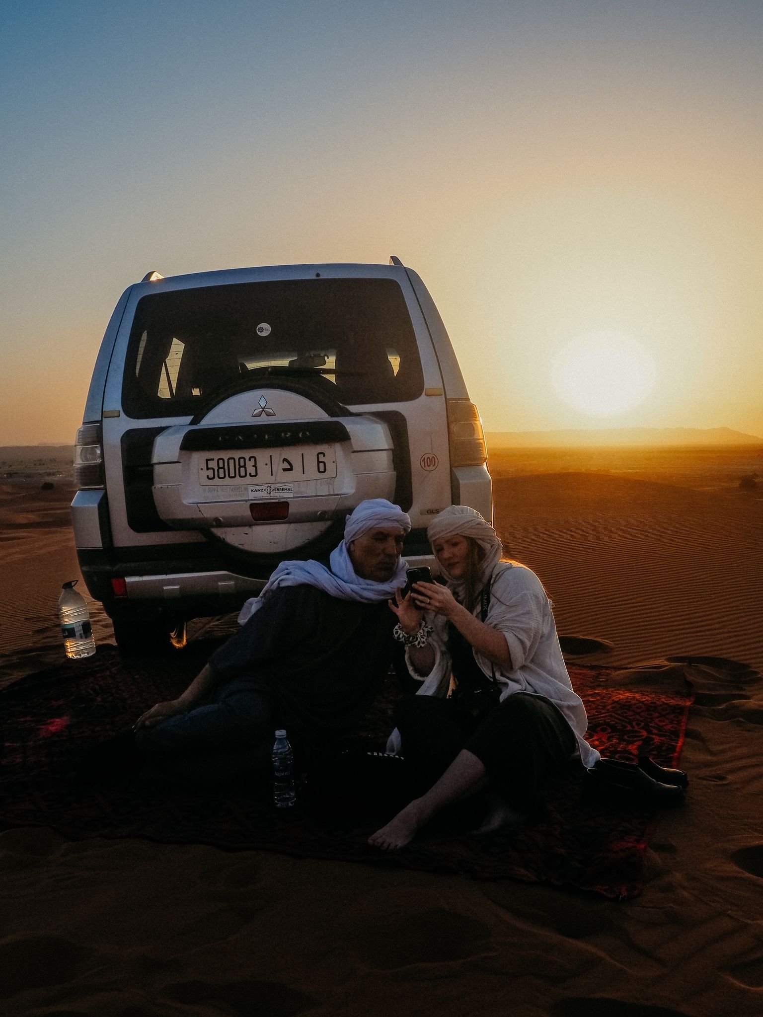 Travelers in desert scarves photographing the sunset beside a 4x4